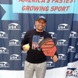 Tarmizi Mawardi memegang bola dan paddle, berfoto di depan backdrop bertuliskan "Olahraga Paling Pesat di AS"