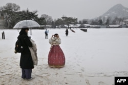 Orang-orang mengenakan pakaian tradisional hanbok berjalan melalui Istana Gyeongbokgung saat hujan salju di Seoul, 26 Januari 2023. (Jung Yeon-je / AFP)
