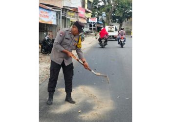 Bhabinkamtibmas Kelurahan Naga Pita Aipda A. Simatupang Tabur Pasir di Tumpahan Solar Jalan Rakutta Sembiring