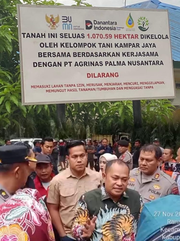 Sejumlah aparat kepolisian bersama perwakilan Kelompok Tani Kampar Jaya Bersama berada di depan papan pengumuman resmi pengelolaan lahan seluas 1.070 hektare di Desa Padang Mutung, Kecamatan Kampar. Kehadiran aparat menegaskan status hukum lahan yang telah disita negara dan diserahkan kepada kelompok tani melalui kerja sama dengan PT Agrinas Palma Nusantara.